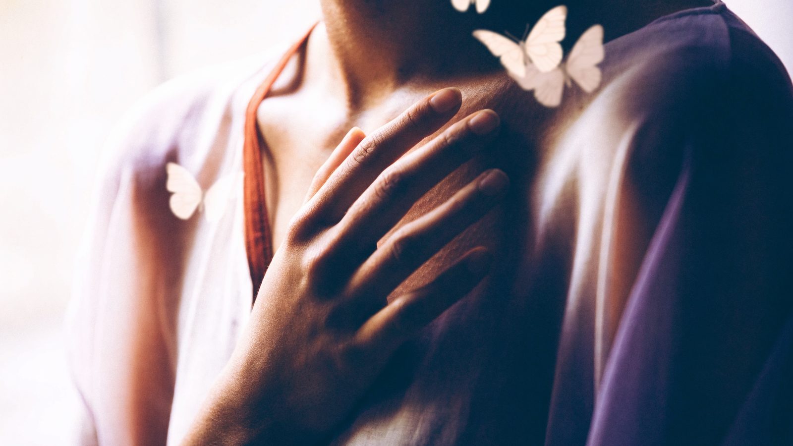 Una mano sobre el pecho, a la altura del corazón, con mariposas alrededor